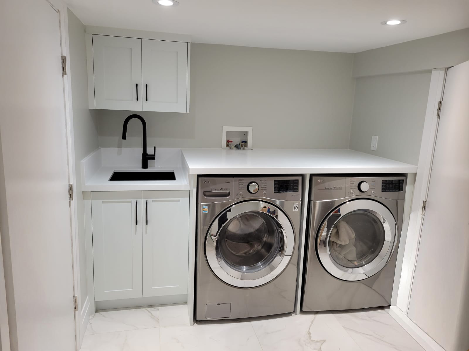 Laundry room with white cabinetry, a black faucet, a washer and dryer, and a countertop above the appliances.