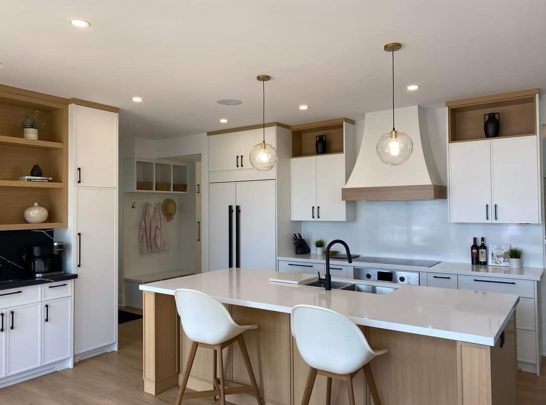 Modern kitchen with white cabinets, a large island with seating, black hardware, pendant lights, and built-in appliances.