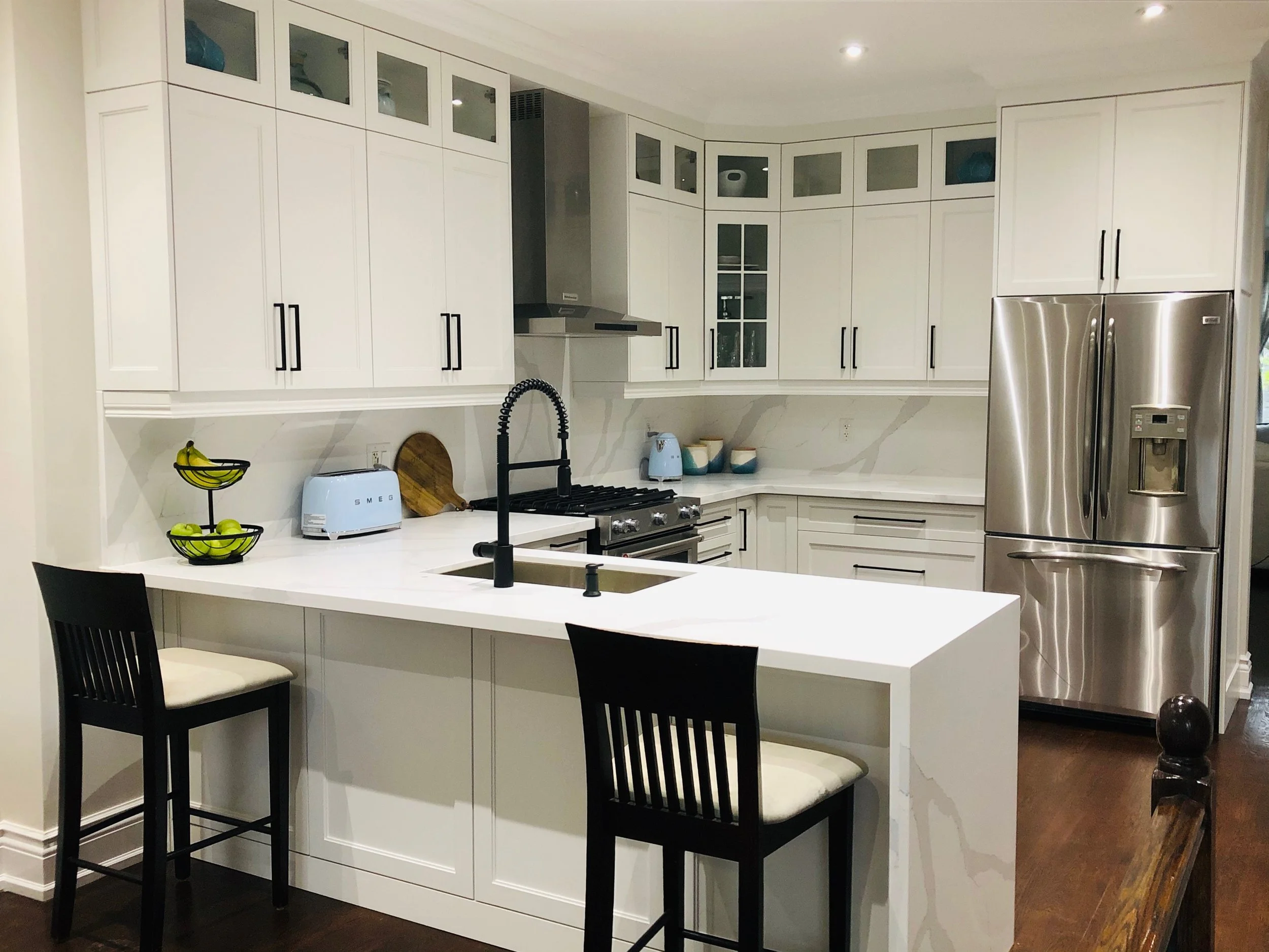 Modern kitchen with white cabinets, a kitchen island with black chairs, a stainless steel refrigerator, and a black faucet over a sink.