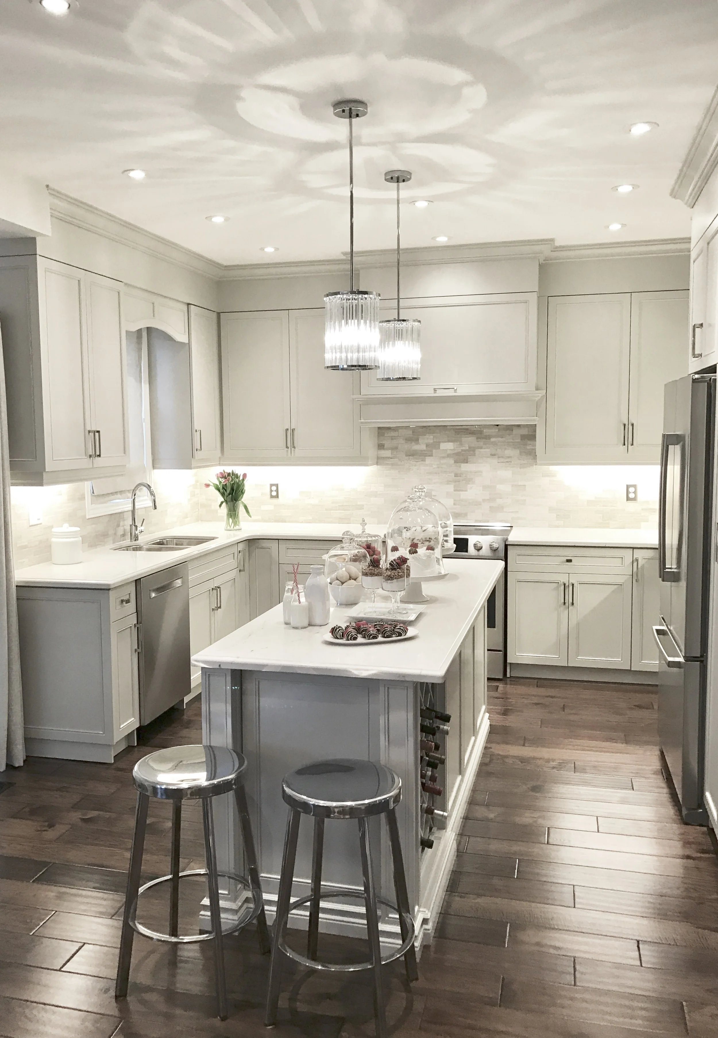 Modern white kitchen with a central island, pendant lights, and barstools, decorated with flowers and treats.