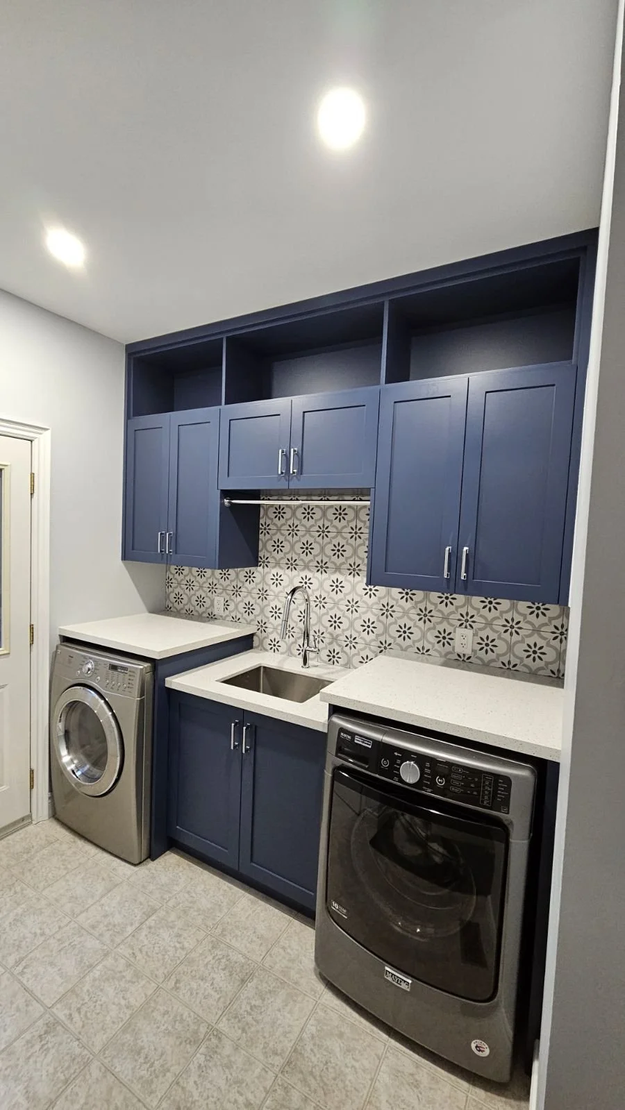 Laundry room with blue cabinets, a white countertop, a sink, patterned tile backsplash, a washing machine, and a dryer.