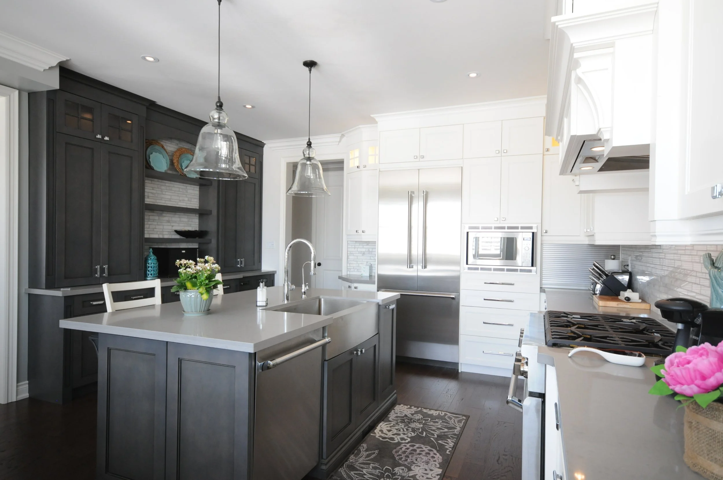Modern kitchen with dark gray cabinets and white countertops, featuring stainless steel appliances, pendant lighting, and a flower arrangement on the island.