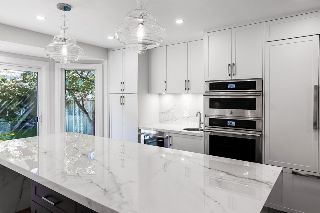 Modern kitchen with white cabinets, marble countertops, black and stainless steel appliances, and pendant lights.