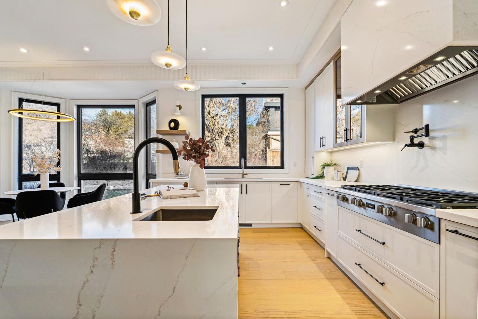 Modern kitchen with white cabinetry, black hardware, a large marble island with a black faucet, black framed windows, and a view of trees outside.