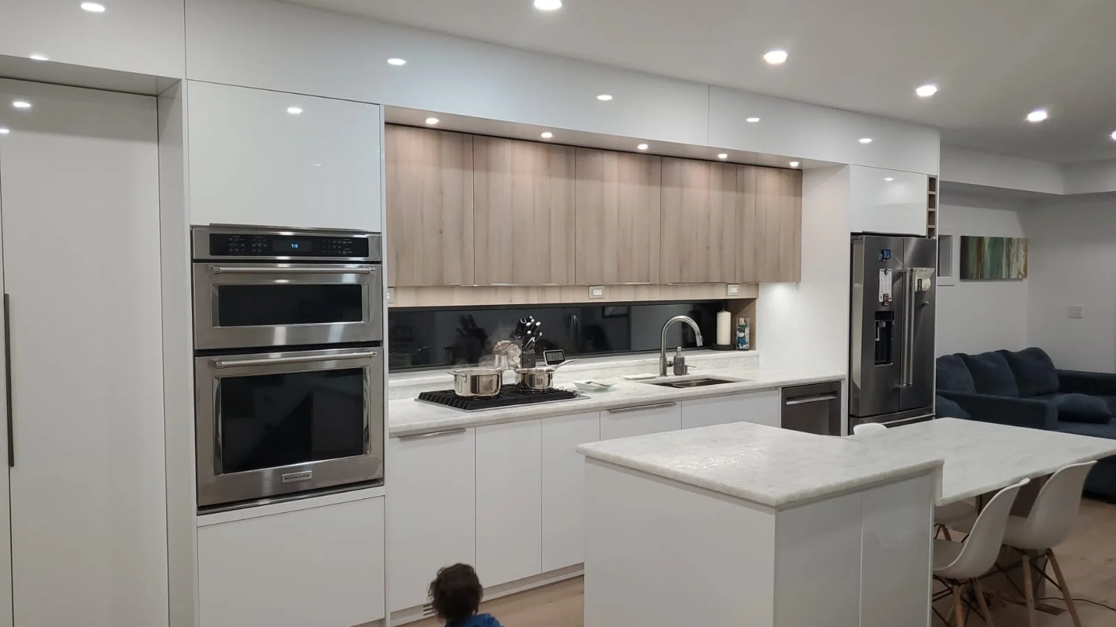 Modern kitchen with white cabinets, stainless steel appliances, marble countertops, and a view of the living room with a sofa.