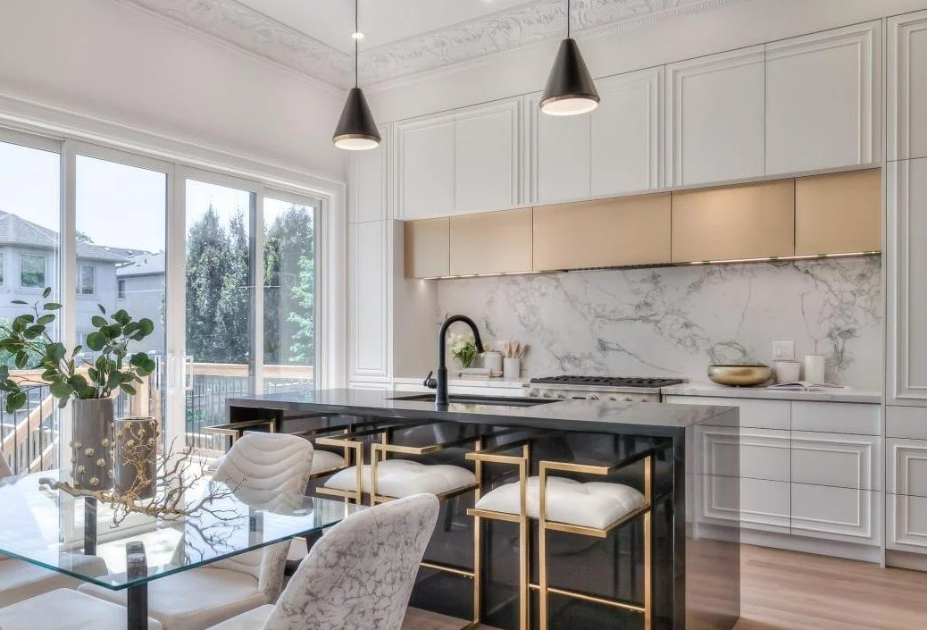 Modern kitchen with white cabinetry, black island with gold accents, and marble backsplash. Includes dining table with white and upholstered chairs, large sliding glass doors, and minimal decorative items.