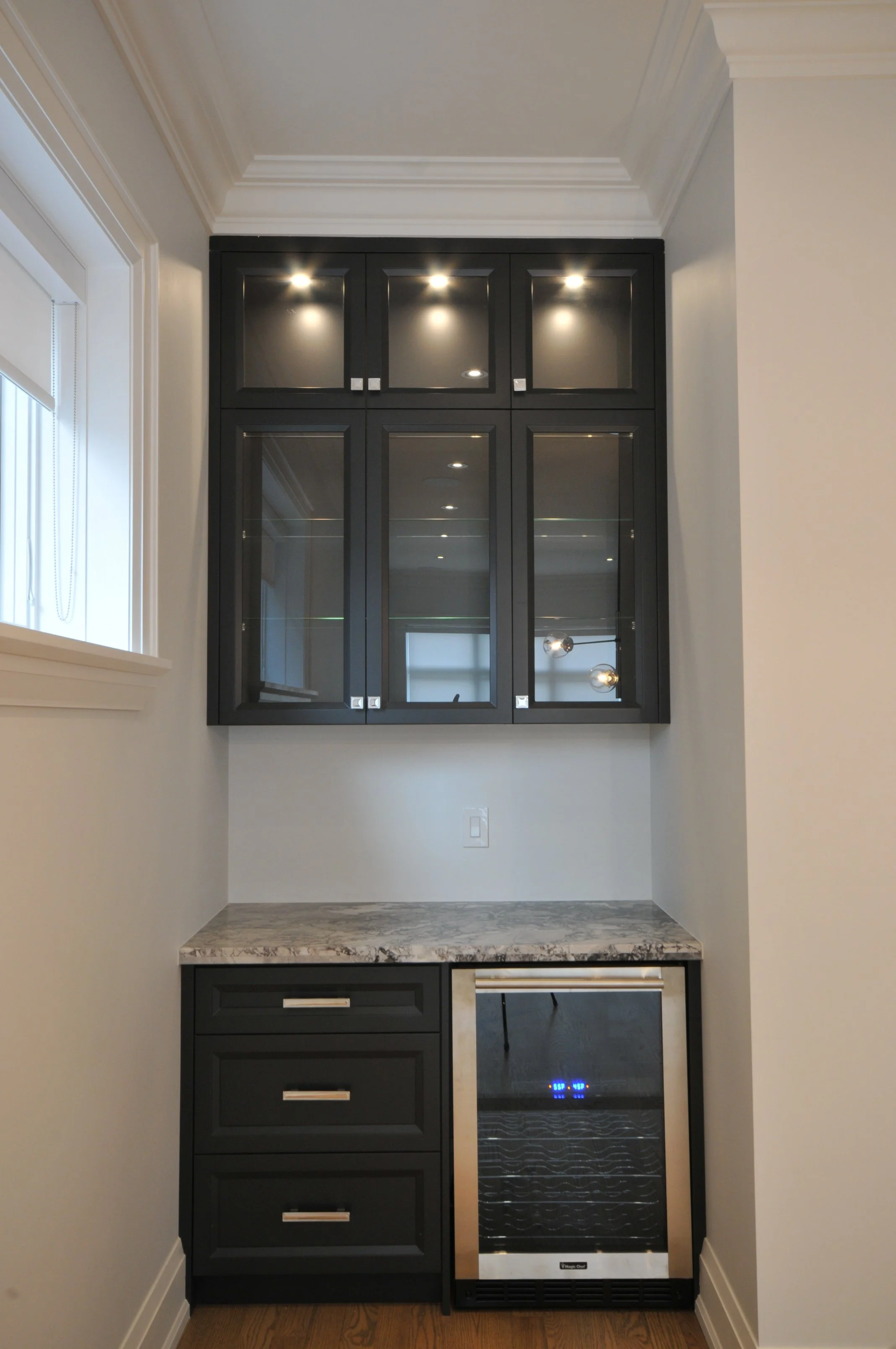 A small bar area with black cabinetry, glass-front upper cabinets, a marble countertop, and a built-in wine cooler below.