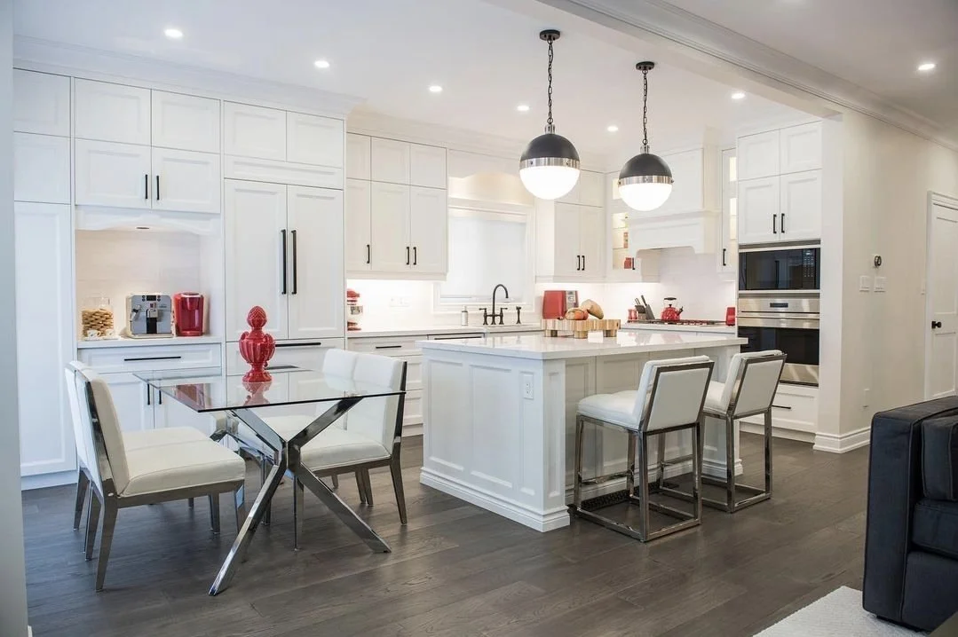 Modern white kitchen with island, pendant lights, dark hardwood floors, and breakfast bar with four white upholstered chairs.