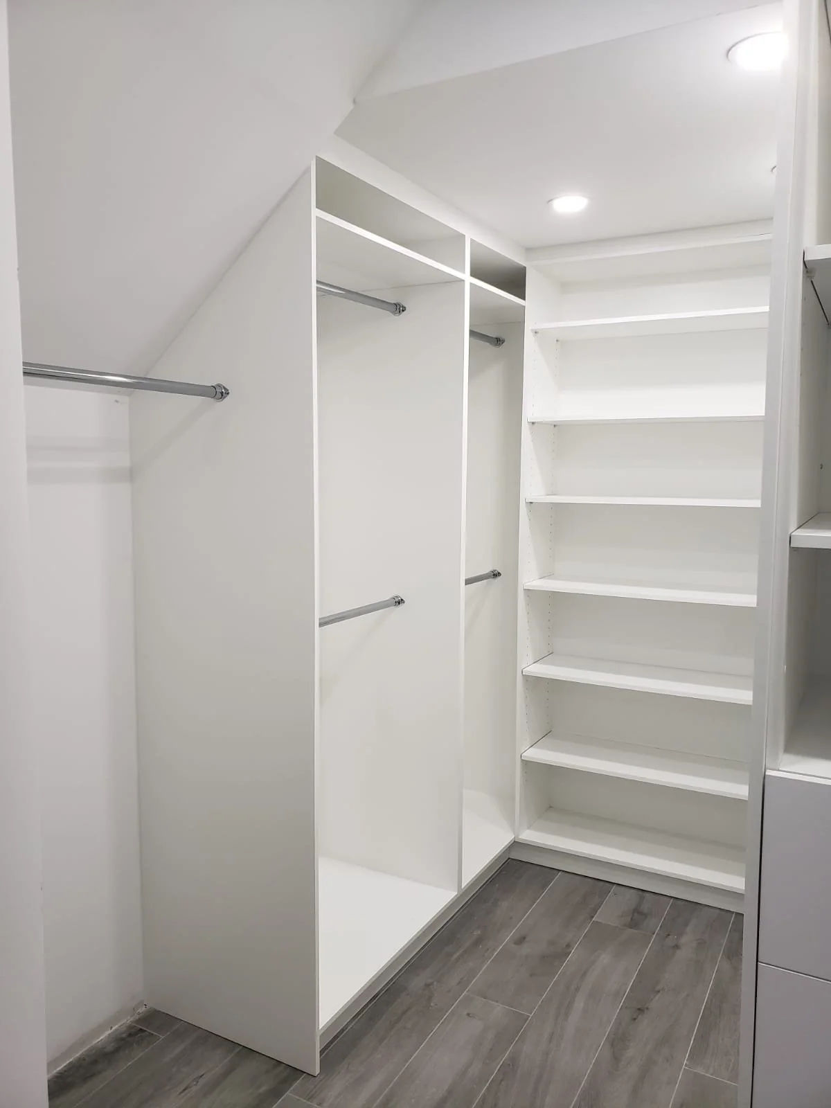 Empty white walk-in closet with shelves and hanging rods, gray wood floor.