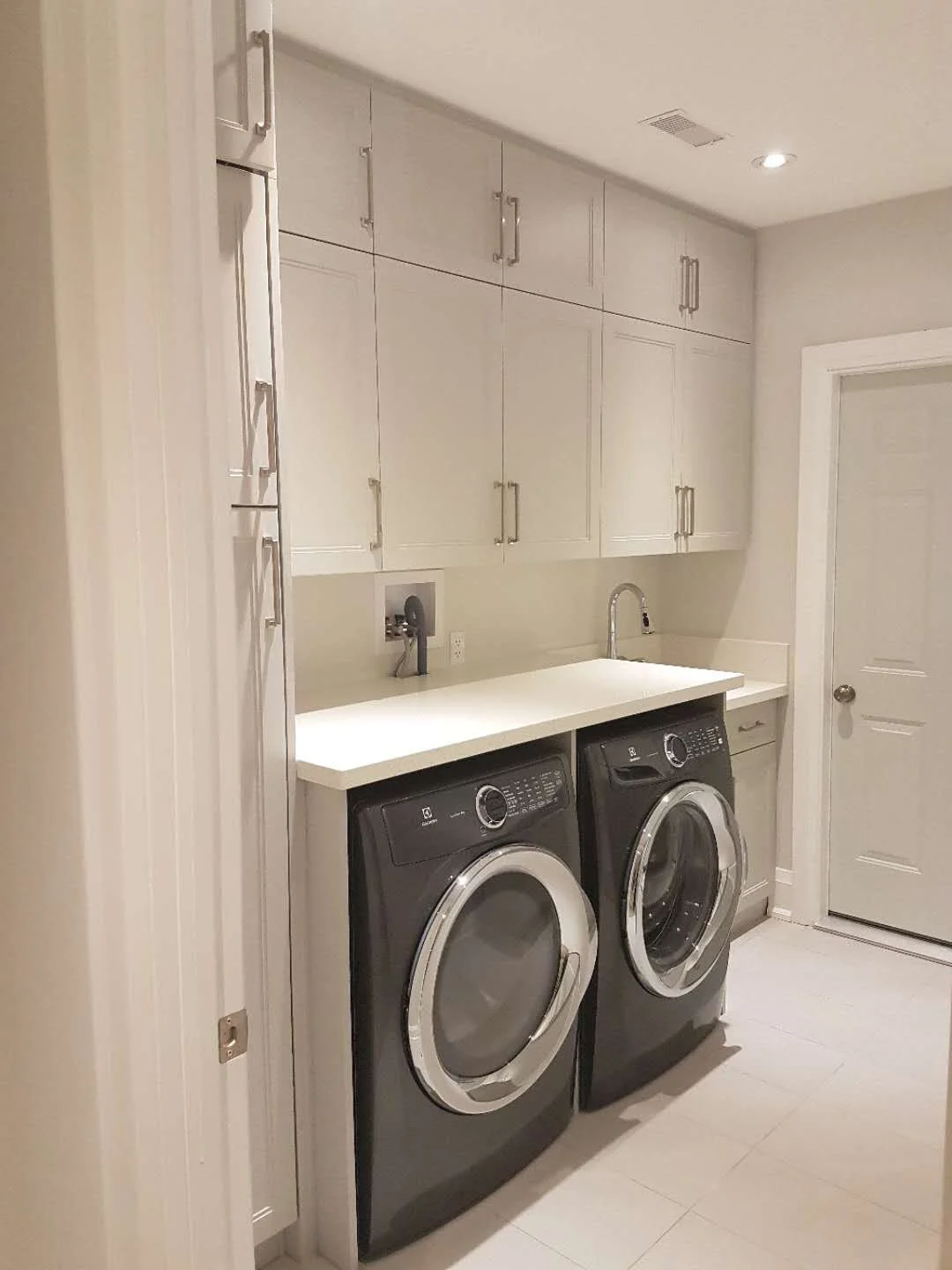 A laundry room with white cabinets, a white countertop, a sink, a faucet, and a washer and dryer in black.