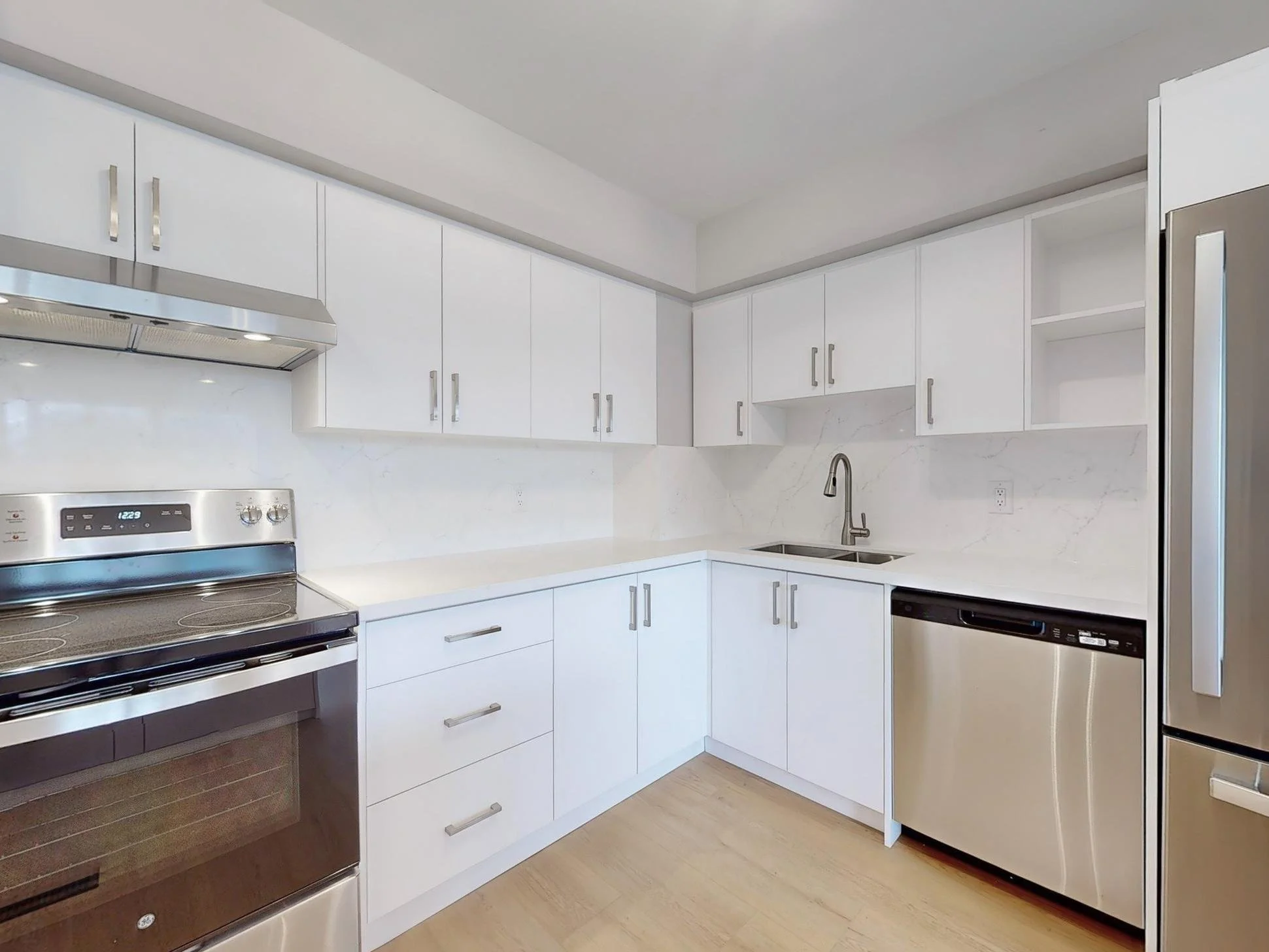 Modern kitchen with white cabinets, stainless steel appliances including a stove, dishwasher, and refrigerator, a marble backsplash, and a stainless steel faucet over a double sink.