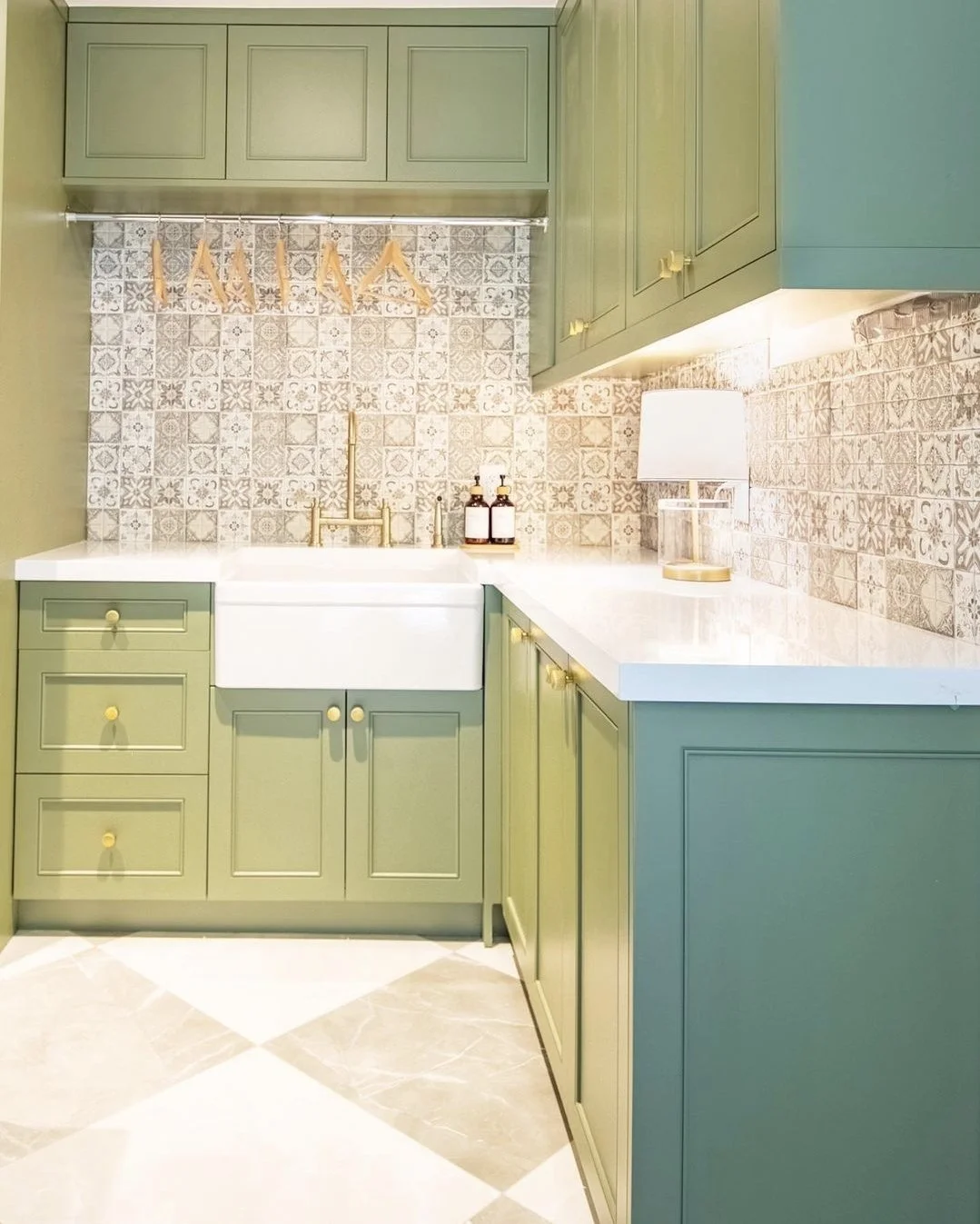 Kitchen with green cabinets, white farmhouse sink, patterned tile backsplash, and a table lamp on the countertop.