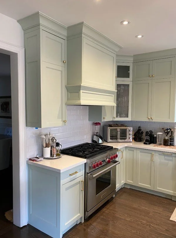 Kitchen with pale green cabinets, stainless steel range, toaster oven, and various small appliances on the counter.