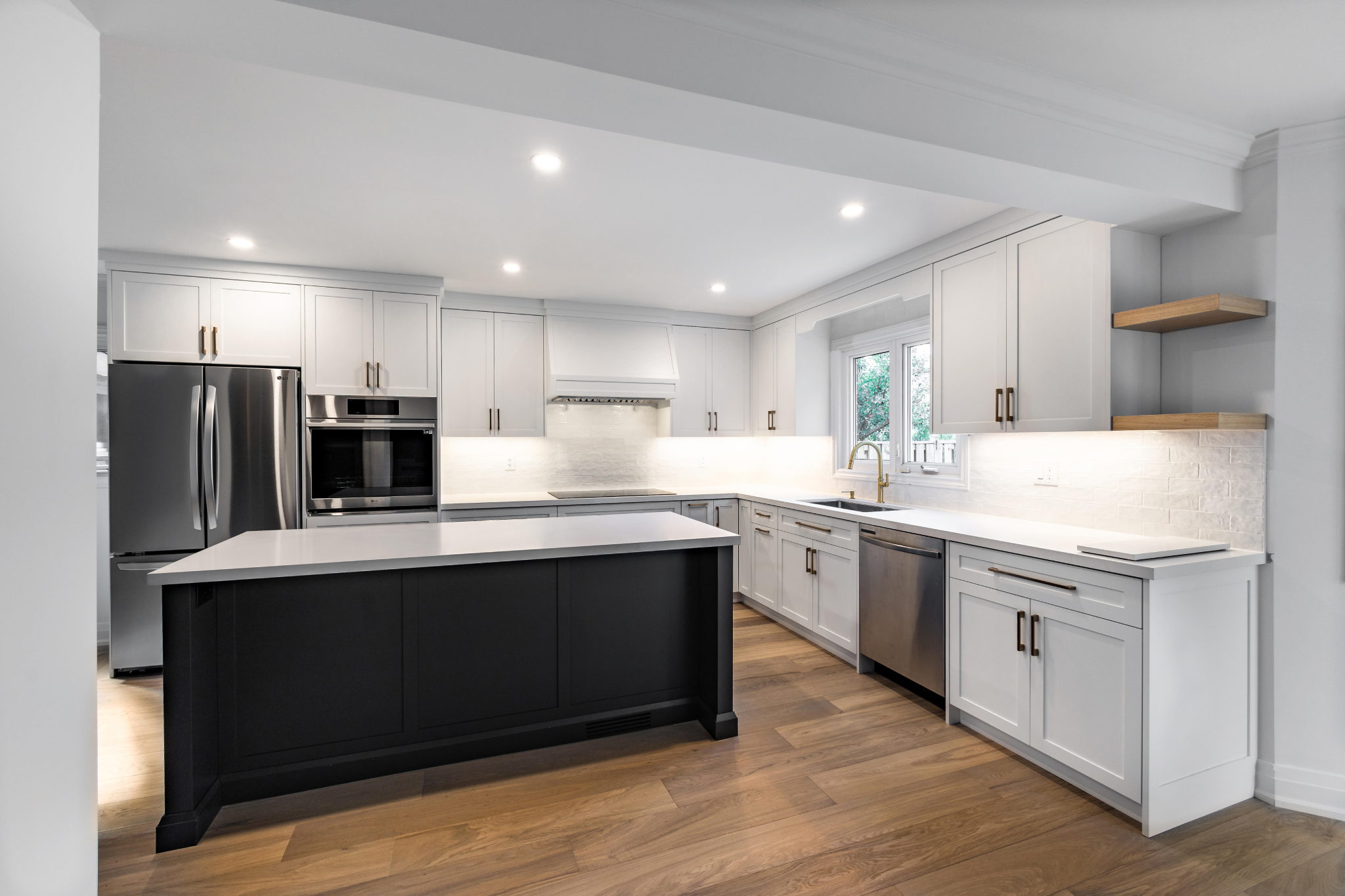 Modern kitchen with white cabinets, a black kitchen island, stainless steel appliances, and wooden flooring.