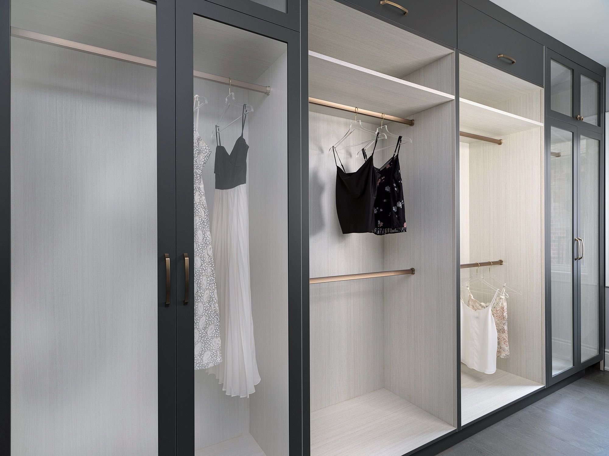 Built-in wardrobe with open sections containing hanging dresses and tops, with some sections closed off with glass doors.