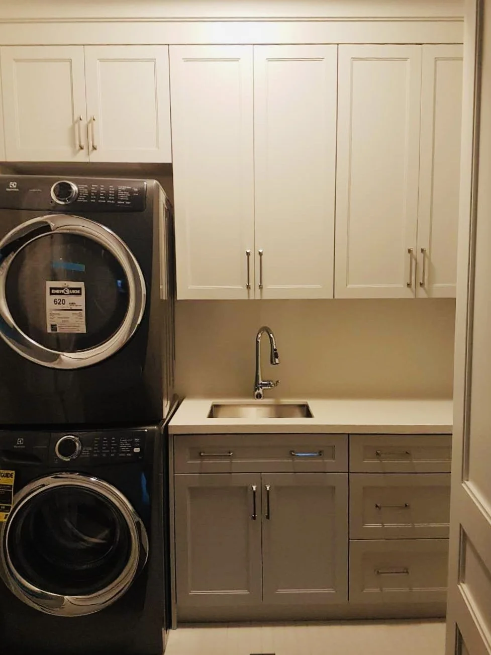 Laundry room with white cabinets, a small sink, and black stacked washer and dryer units.