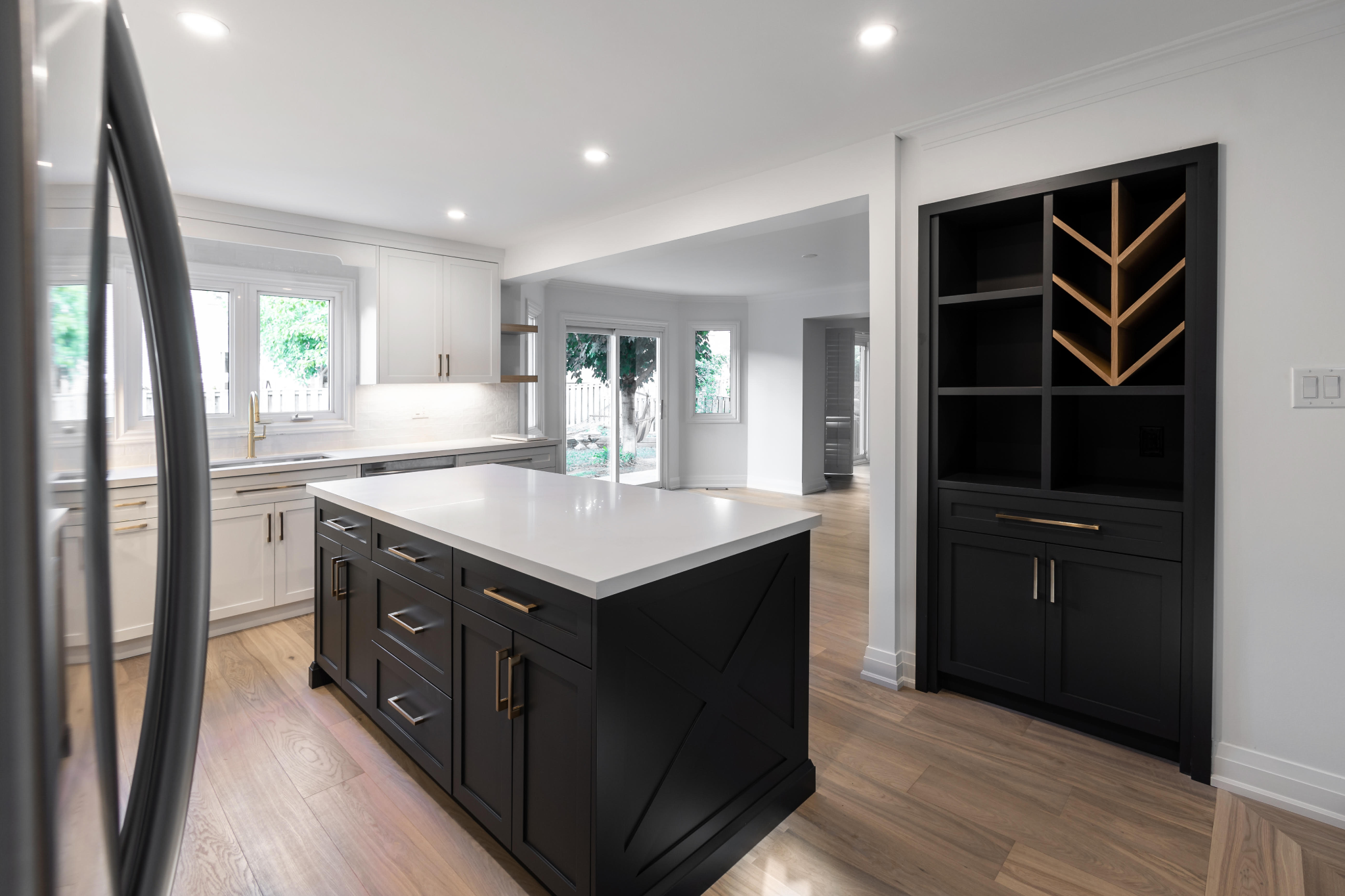 Modern kitchen with white cabinets, a kitchen island, black cabinetry, large windows, and hardwood floors.