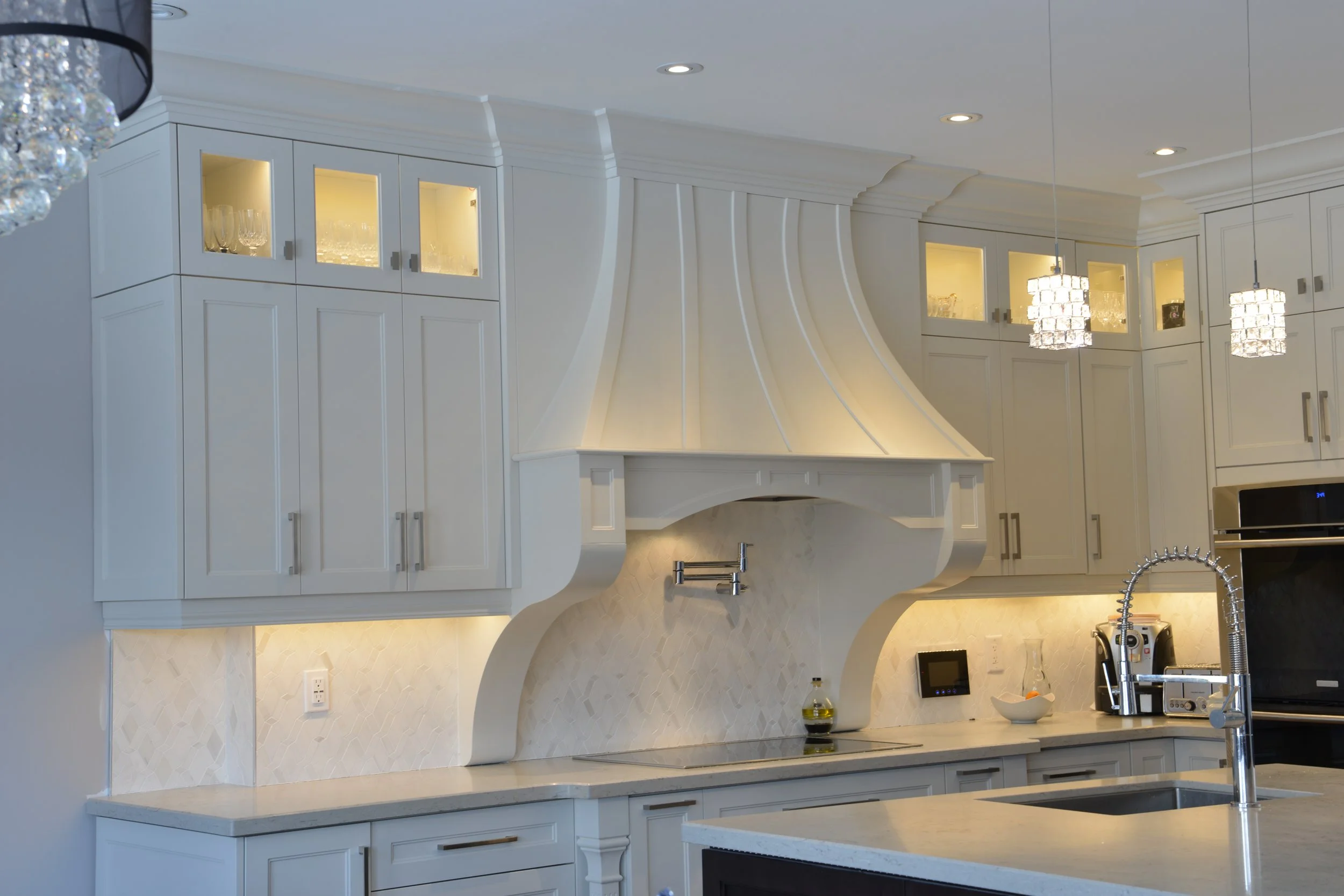 A modern white kitchen with decorative cabinetry, pendant lights, and a built-in oven.