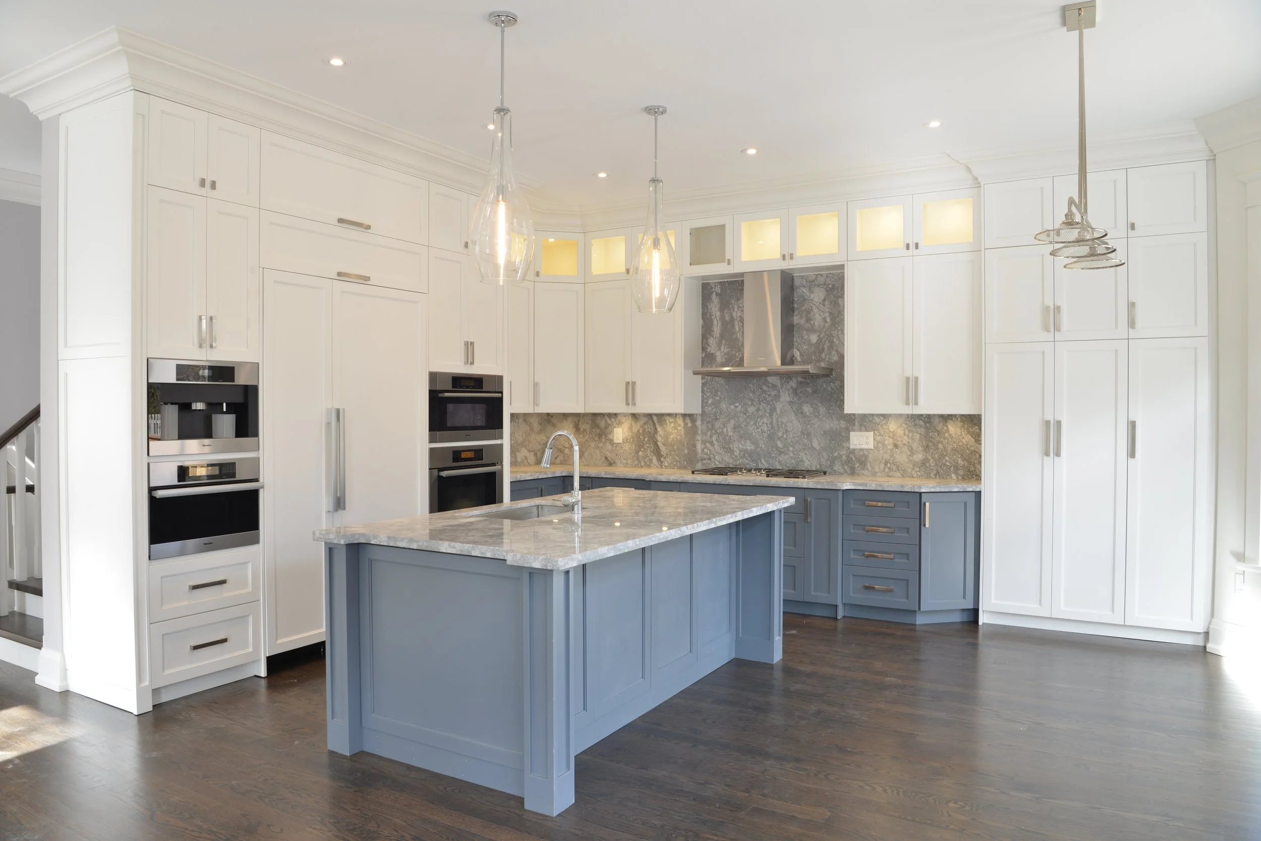 Modern kitchen with white upper cabinets, blue lower cabinets, a marble countertop island, stainless steel appliances, gray marble backsplash, and pendant lighting.