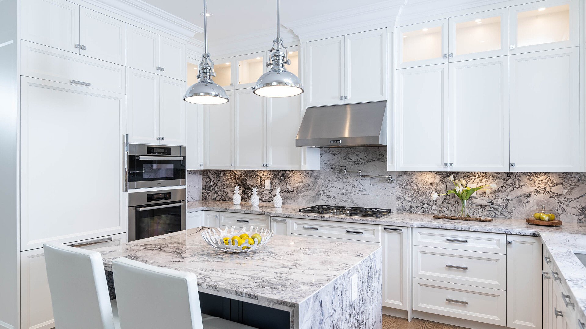 Modern white kitchen with marble countertops, stainless steel appliances, and pendant lighting.