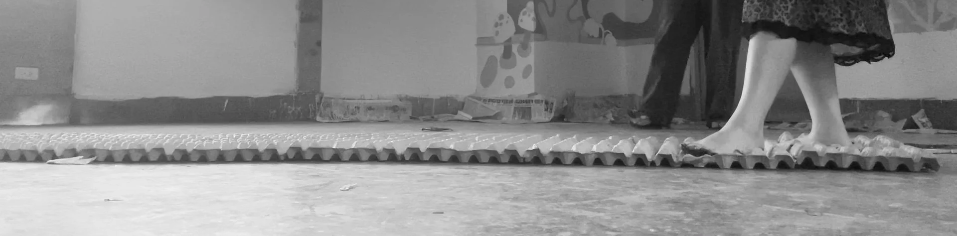 Footwear and a person's legs as they walk on a textured outdoor surface, with a background of a wall and some wall art.