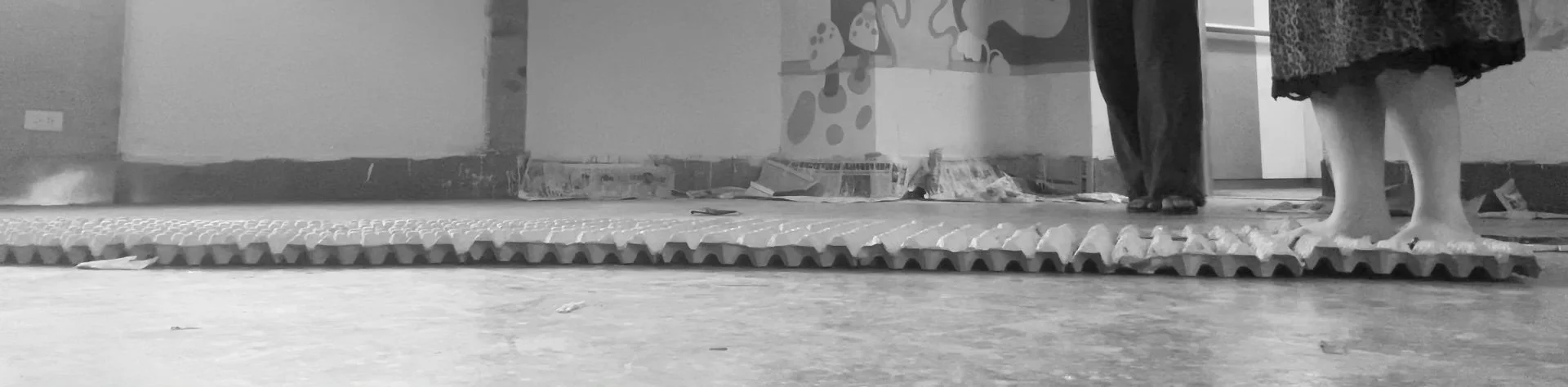 People standing barefoot on a textured floor mat in an indoor space with walls and some artwork.