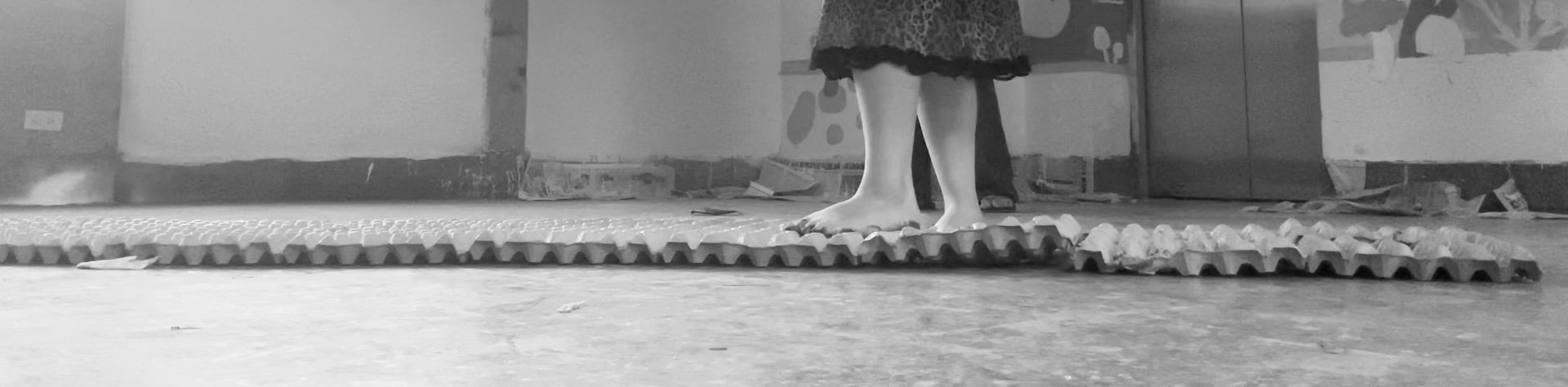 Child standing barefoot on foam mats in a room with patterned wallpaper.