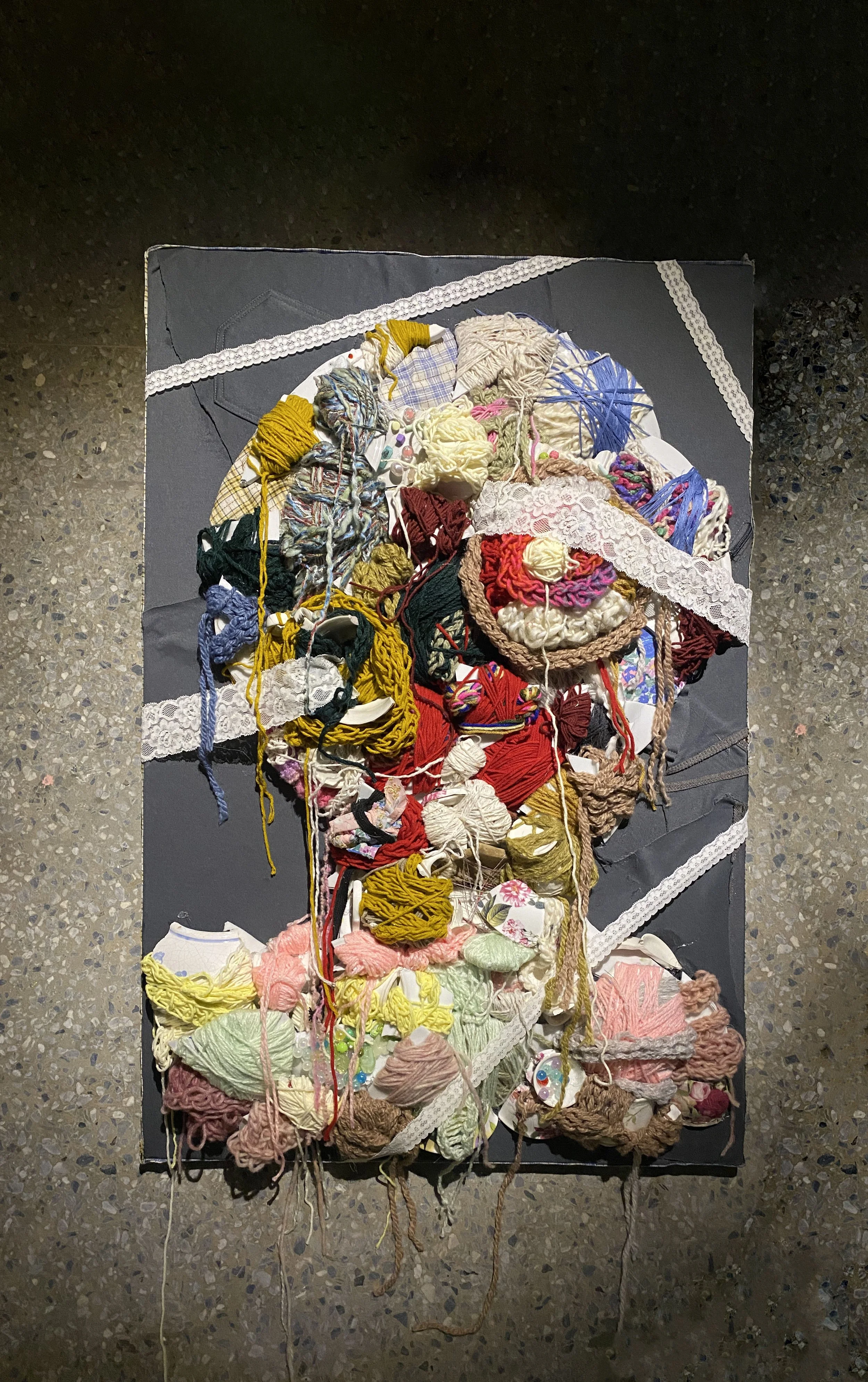 Mixed colorful yarns, textiles, and lace arranged on a dark surface, forming a textured and abstract art piece.