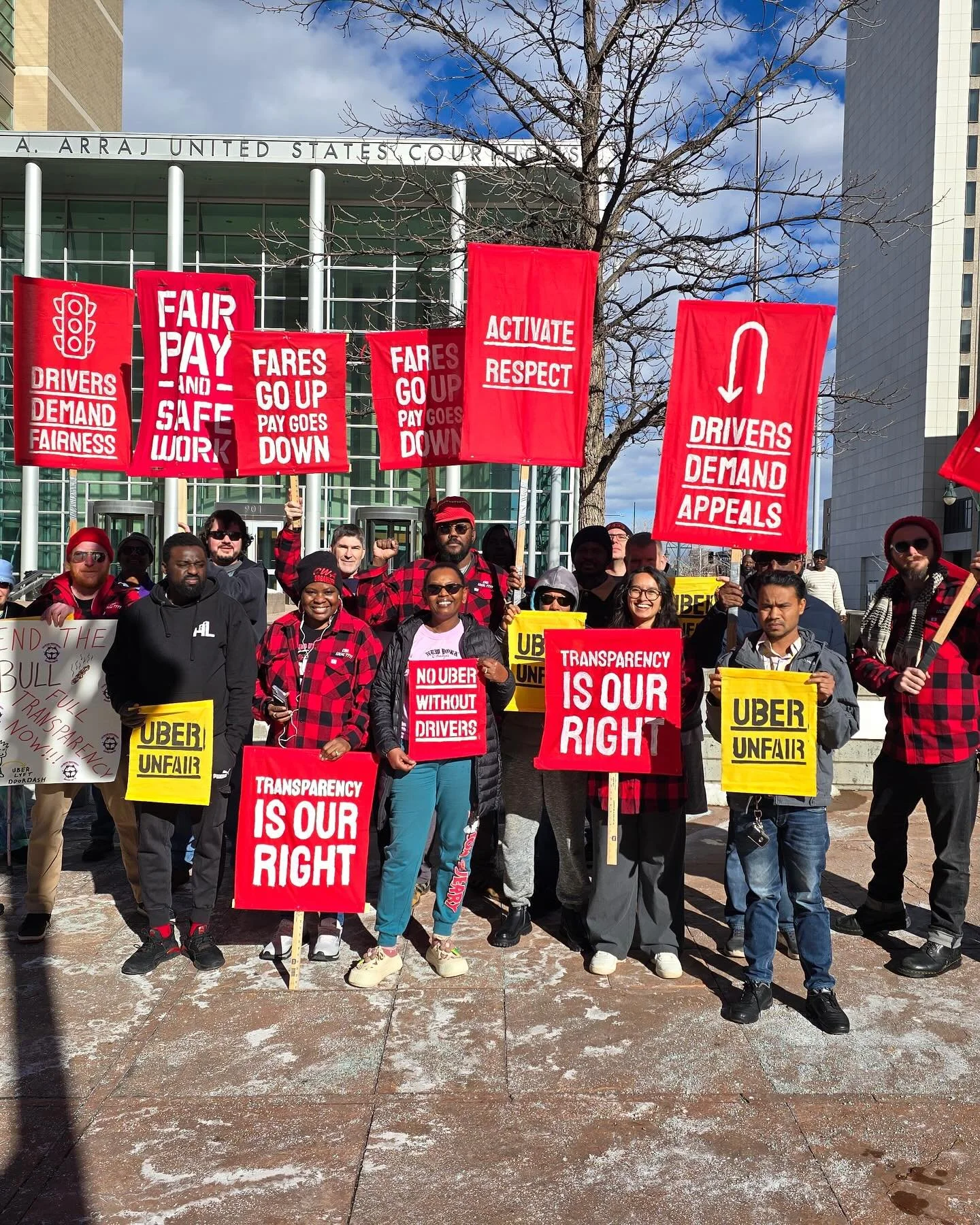 Protesters holding signs and banners advocating for drivers' rights, transparency, and fair pay outside a government building.