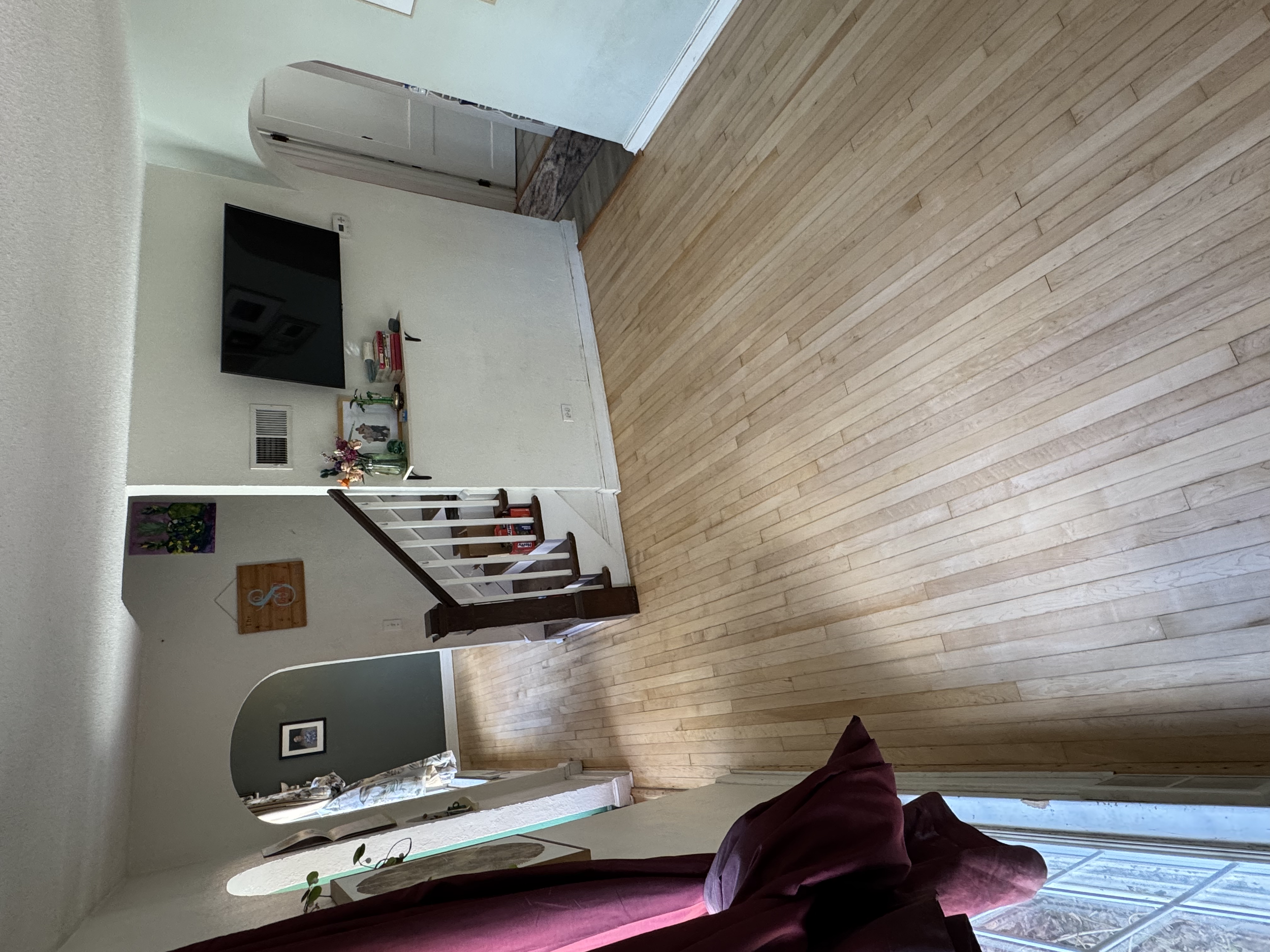 Living room with a wooden floor, staircase, TV mounted on the wall, decorative items, and a window with curtains.