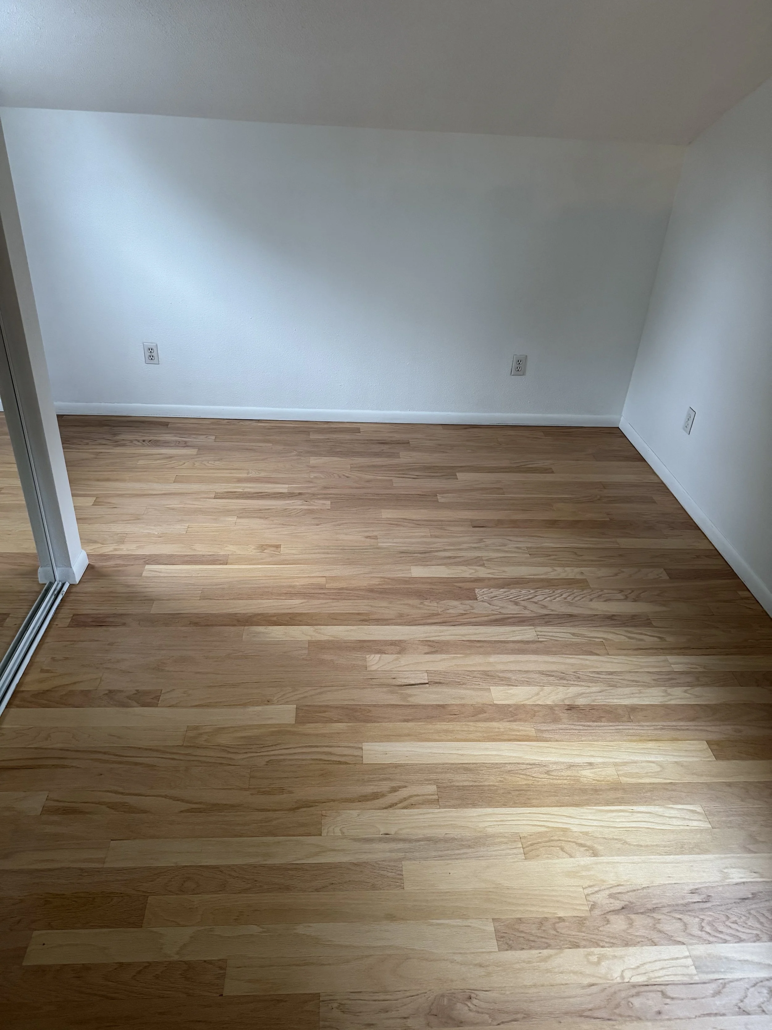 Empty room with light-colored hardwood floors, white walls, and multiple electrical outlets.