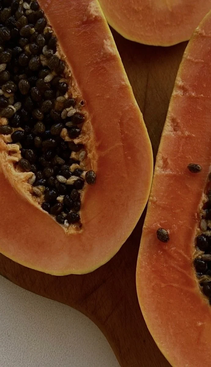 Close-up of sliced papayas with orange flesh and black seeds on a wooden cutting board.