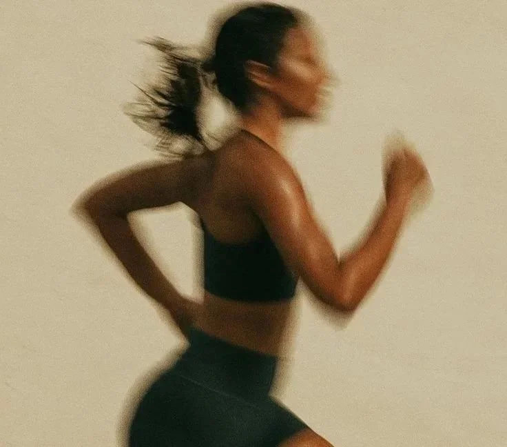 Blurry image of a woman running indoors, wearing a black sports bra and black shorts.
