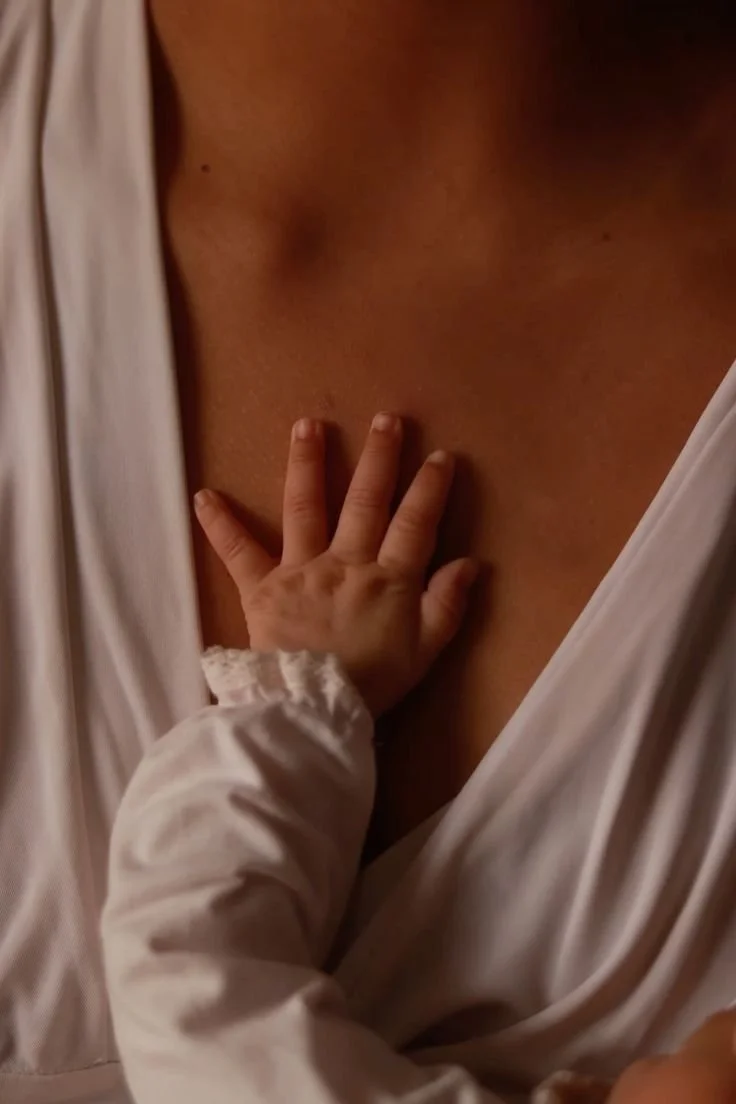 A baby’s hand resting on a woman's chest, partly covered by a white garment.