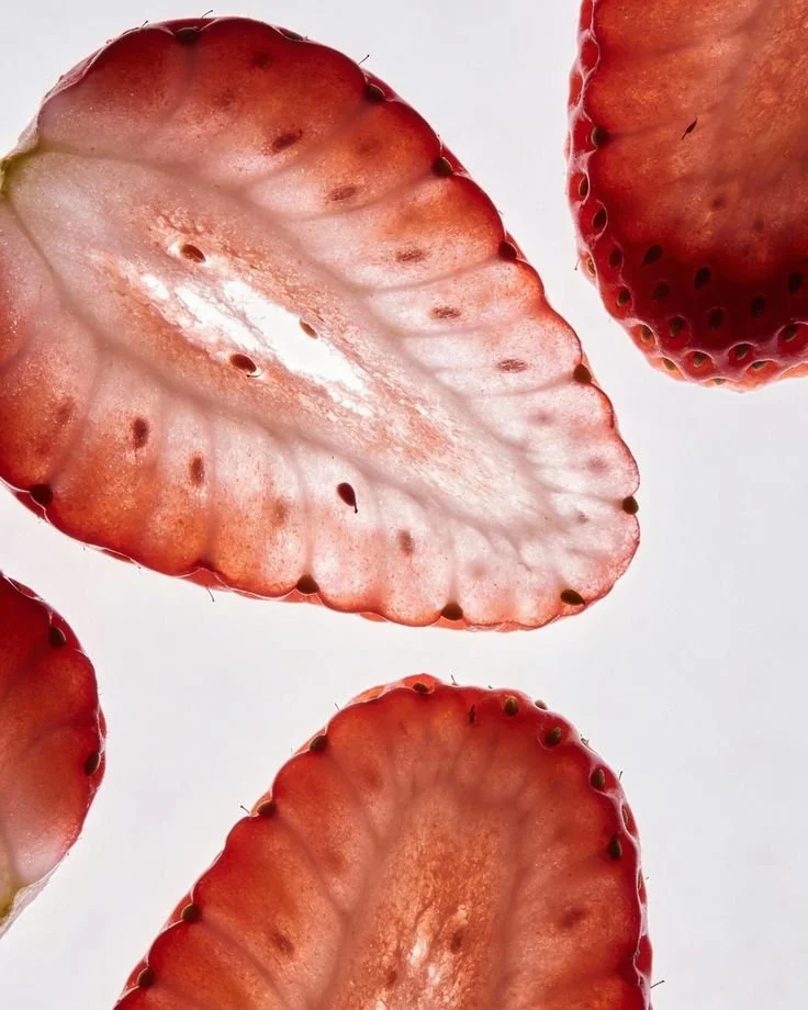Close-up of sliced strawberries with red flesh and small seeds, set against a white background.