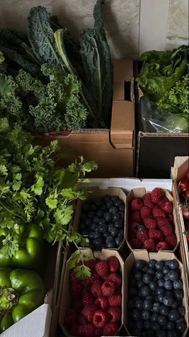Fresh green leafy vegetables, turmeric, cilantro, and berries in small cardboard boxes at a market stand.