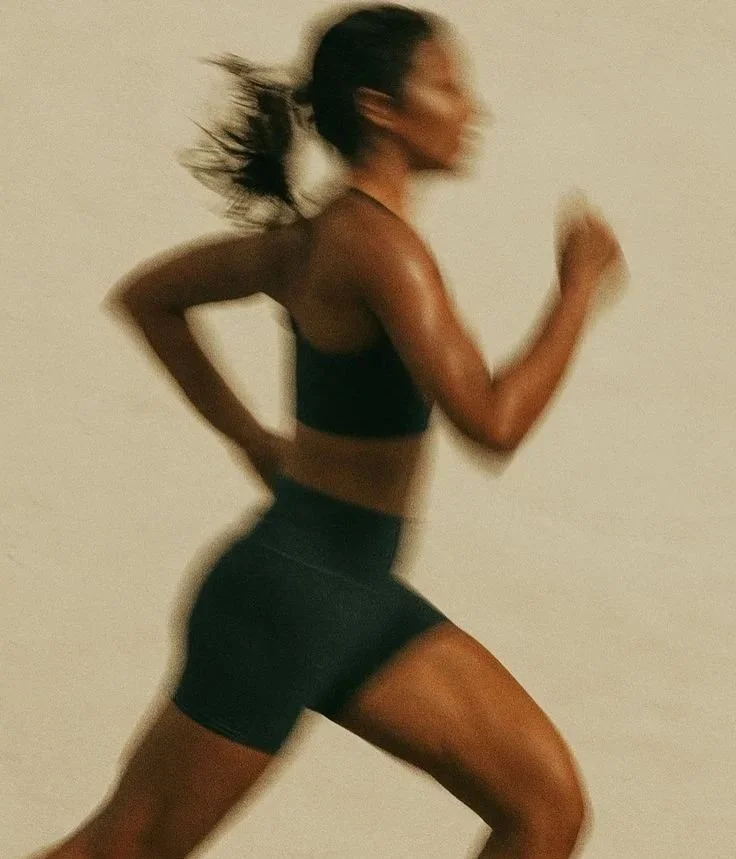 A woman running indoors in athletic wear, with her hair pulled back and in motion.