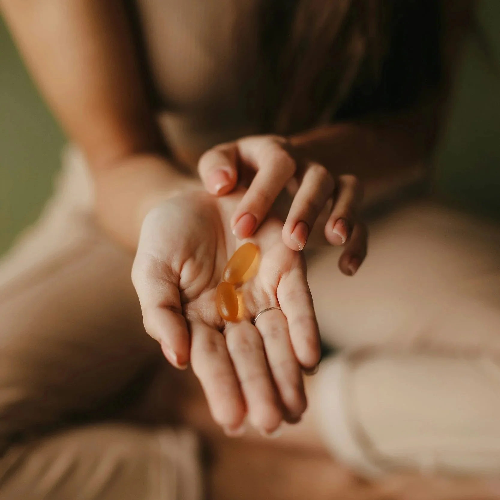 Close-up of two hands holding each other, with one hand having a pill. The background is blurred.