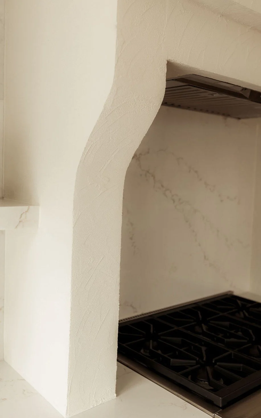 Close-up of a kitchen countertop with a small archway and a gas stovetop. The wall and countertop are white with subtle marble veining.