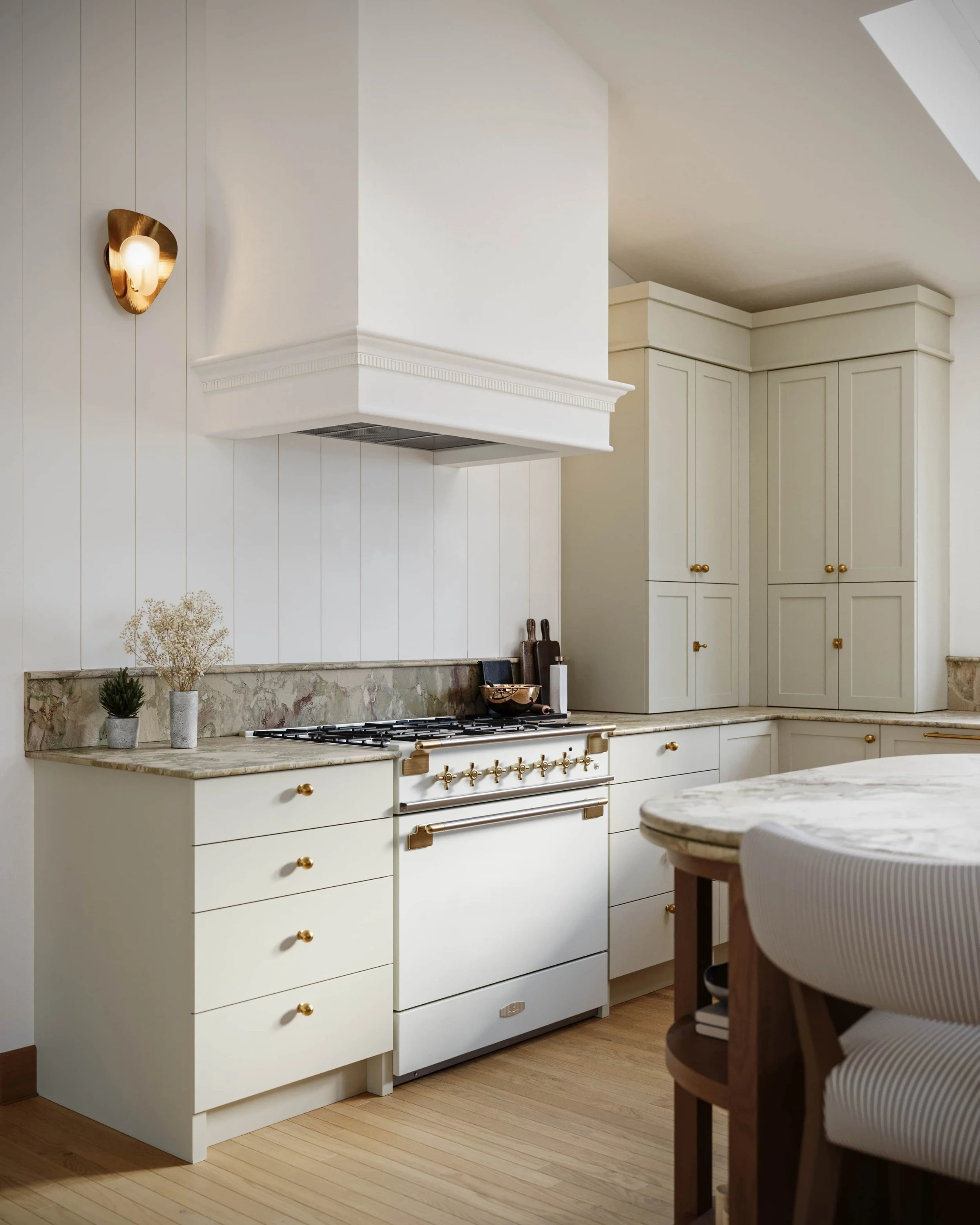 A modern white kitchen with gold accents, a marble countertop, a stove, and an island with an upholstered chair.
