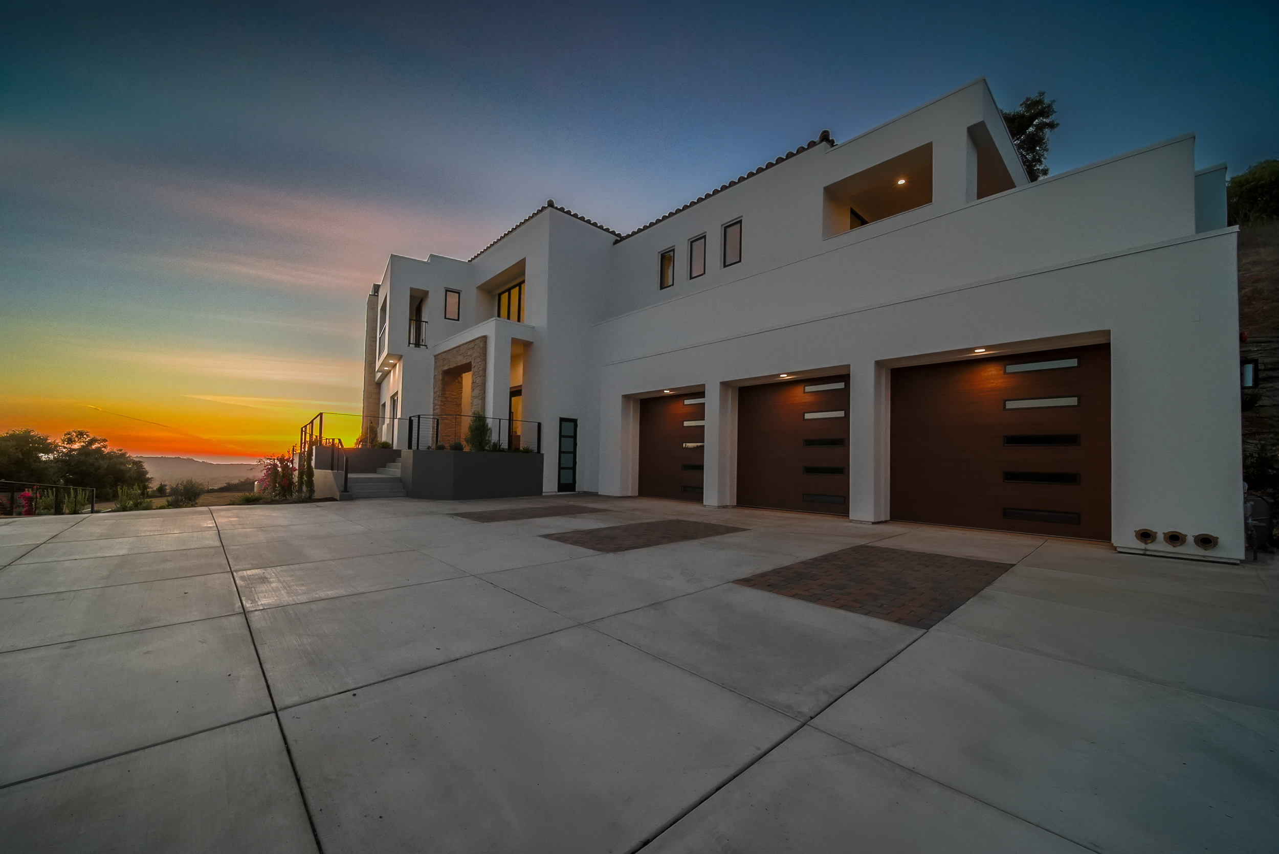 Modern white house with three garages, balconies, and steps leading to front door at sunset.