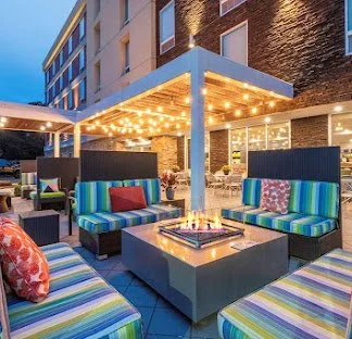 Outdoor rooftop lounge area with colorful striped seating, decorated with string lights, in front of a brick building