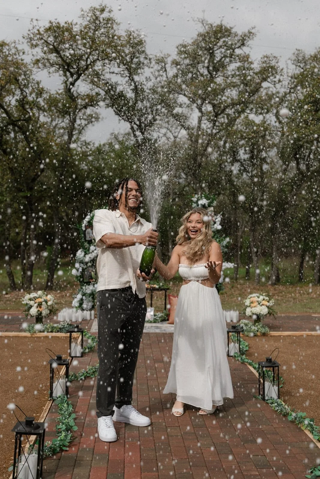 A couple celebrating their engagement with champagne outdoors at Wrenwood Ranch in Fredericksburg texas