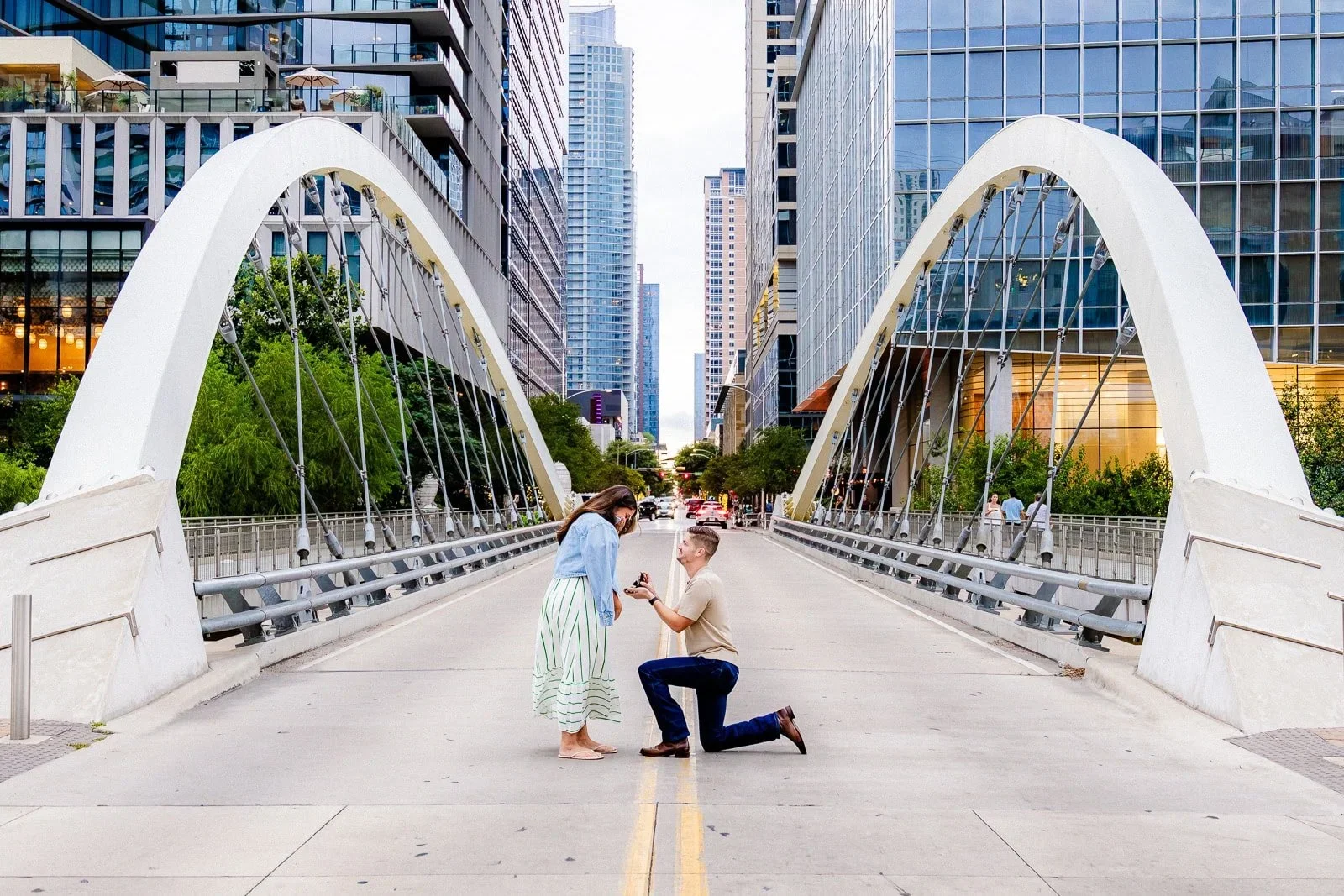 man kneeling down proposing to woman on bridge in Austin, TX