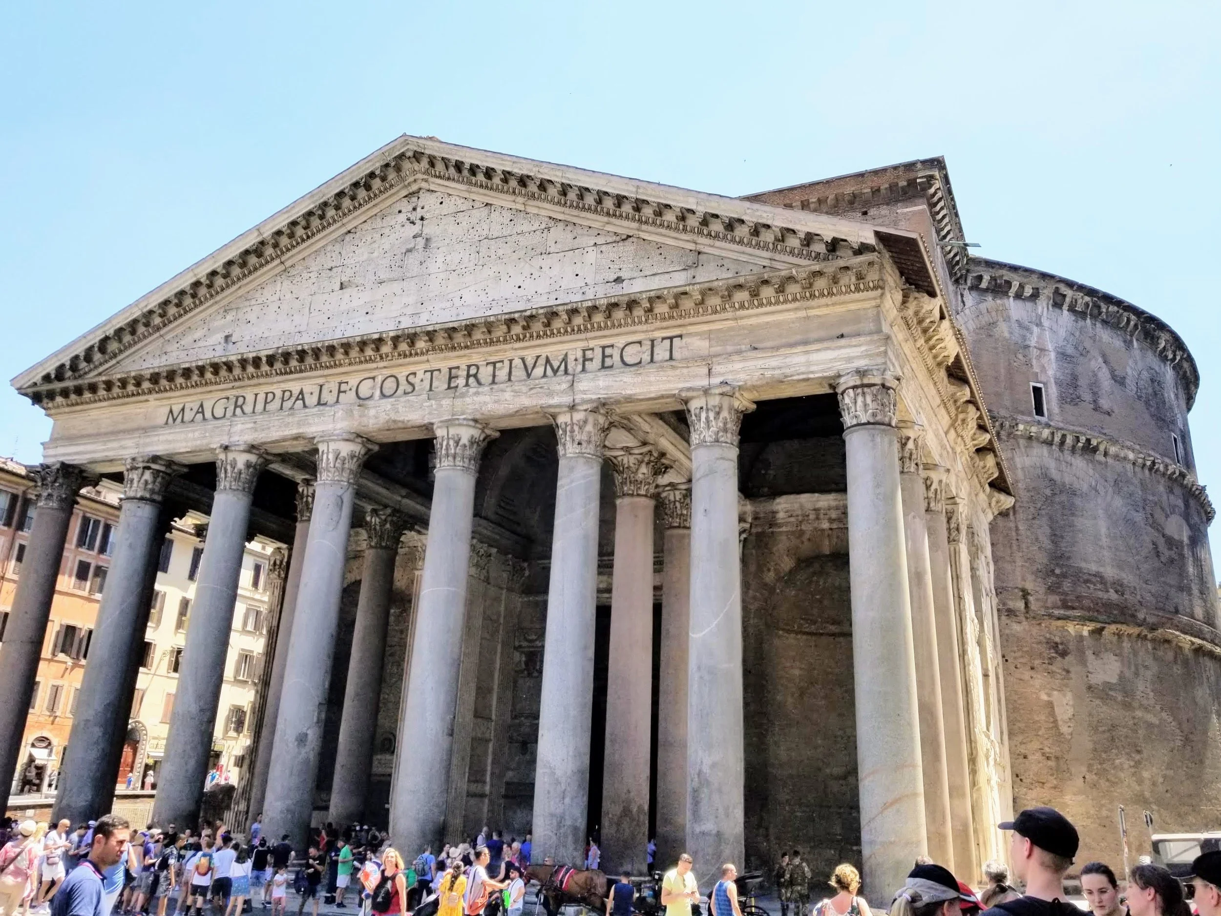Ancient Roman temple with large columns and Latin inscription, surrounded by tourists in Rome, Italy.