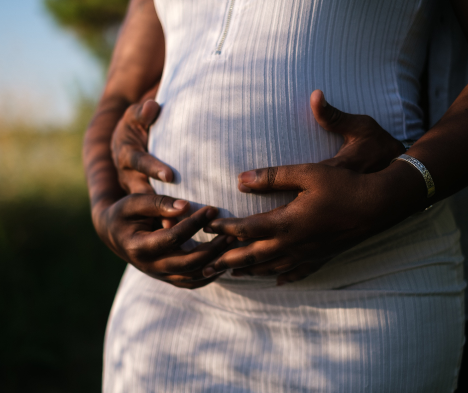Close-up of a pregnant woman's belly being held by two dark-skinned hands.