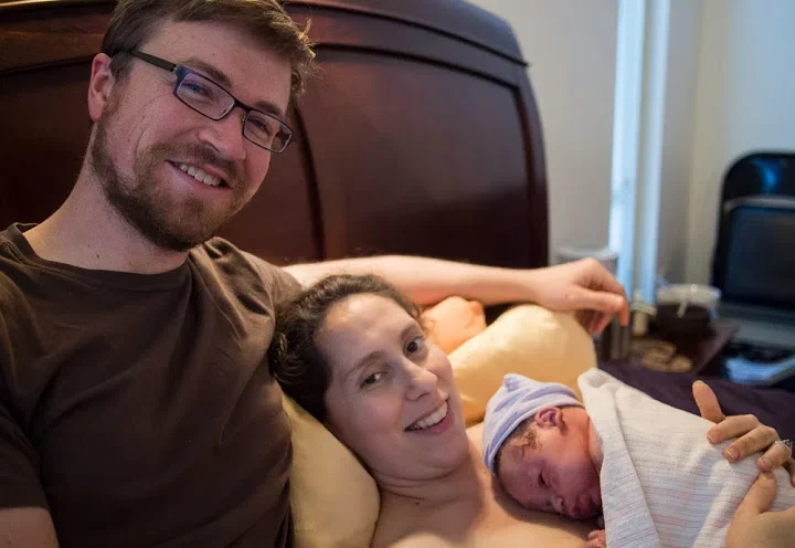 A happy family with a man, woman, and newborn baby lying in bed together.