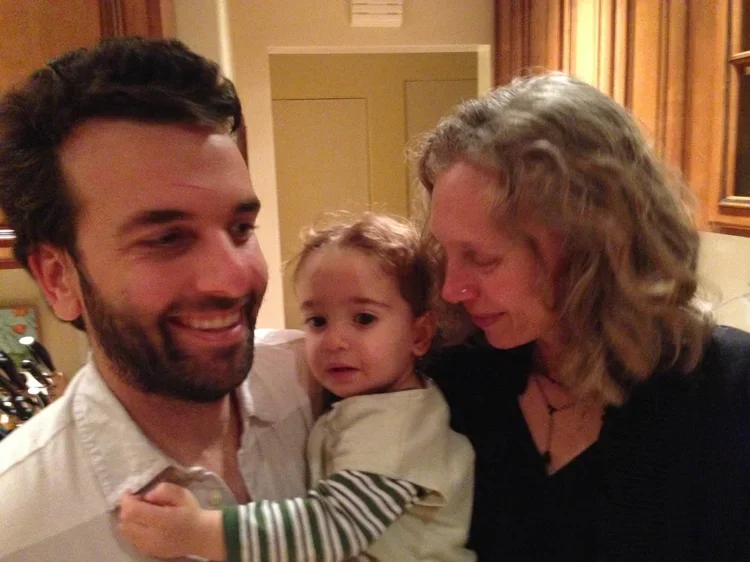 A happy family of three indoors, with a man, woman, and a young child, all smiling and close together.