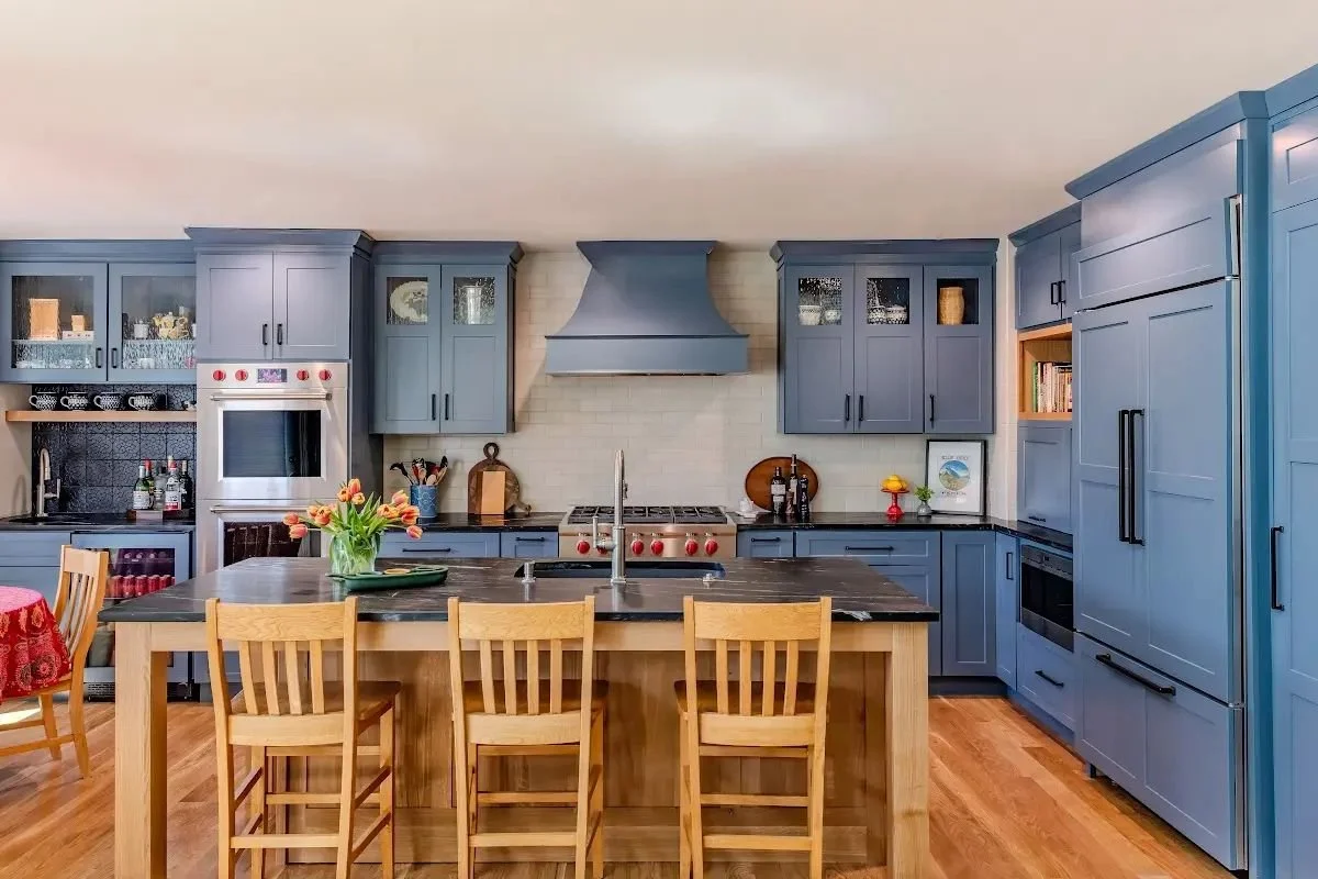 Kitchen design reference: blue cabinets and range hood with a dark island countertop and wood seating.