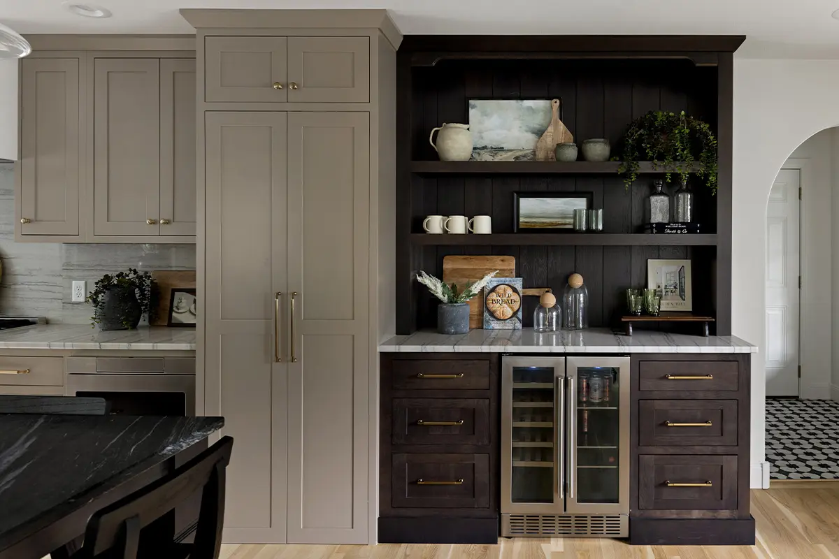 A kitchen with beige upper cabinets and a dark wood open shelving unit that holds decorative items, dishes, and a small wine cooler with glass doors.
